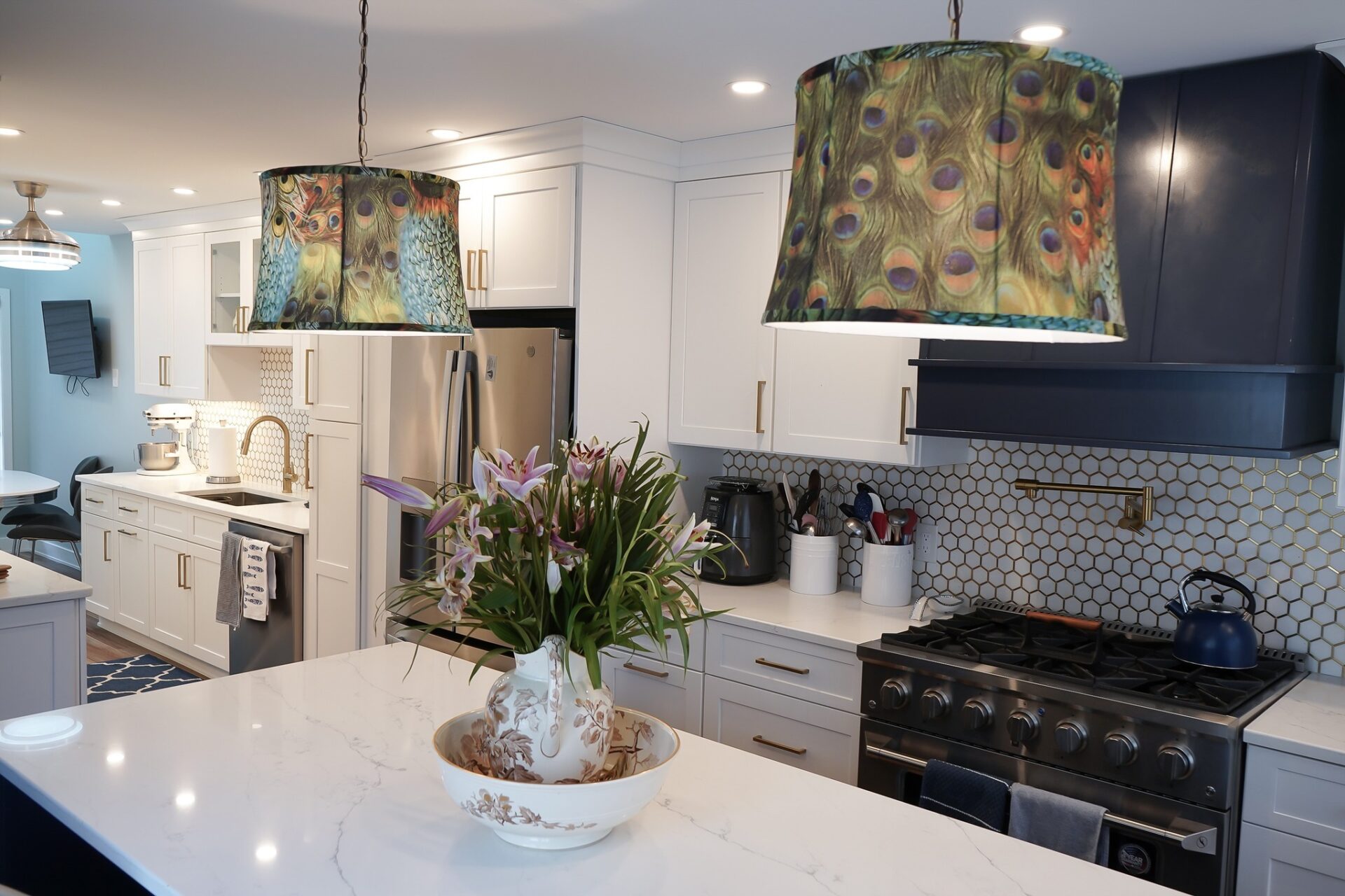 Stylish kitchen remodel in Newington, CT featuring white shaker cabinets, peacock feather pendant lights, gold hardware, and a luxury gas range with honeycomb tile backsplash.