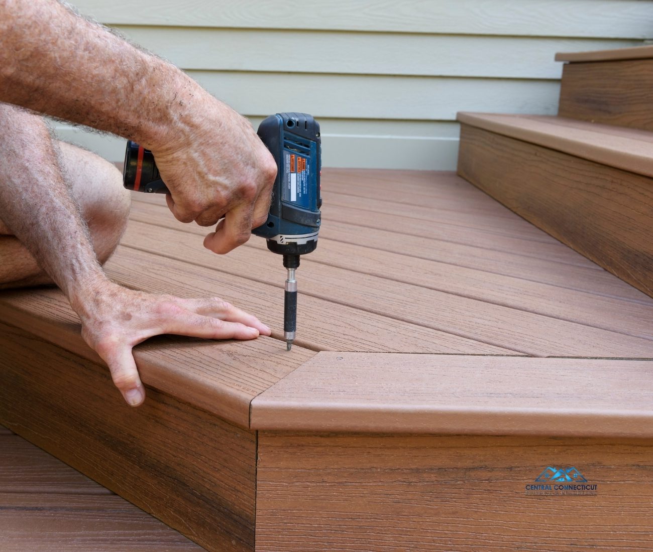 Close-up of a contractor’s hands using a power drill to secure composite decking boards during the construction of a new deck in Berlin, CT — built by Central Connecticut Building & Remodeling.