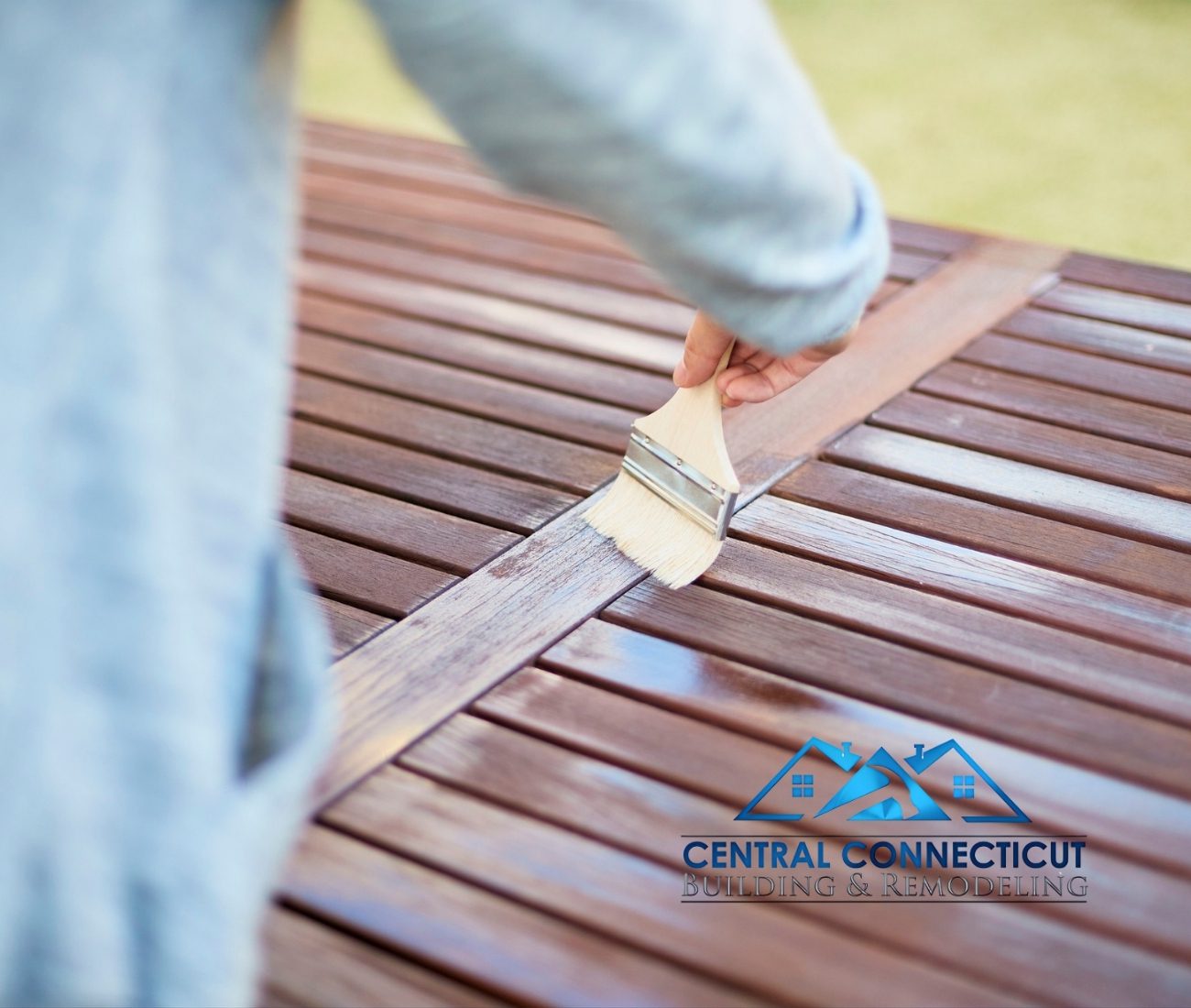 Close-up of a hand using a brush to apply protective stain to a wooden deck surface — Central Connecticut Building & Remodeling preserving and finishing a deck in Newington, CT.