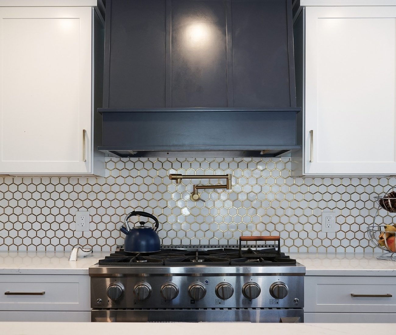 Modern kitchen remodel featuring a stainless steel gas range, gold hexagonal tile backsplash, navy range hood, and white cabinetry — completed by Central Connecticut Building & Remodeling in Newington, CT.